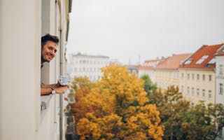 Mann lener seg ut av vindu på leilighet med trær utenfor
