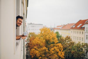 Mann lener seg ut av vindu på leilighet med trær utenfor