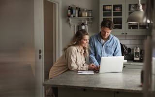 Kvinne og mann ser på laptop i et kjøkken