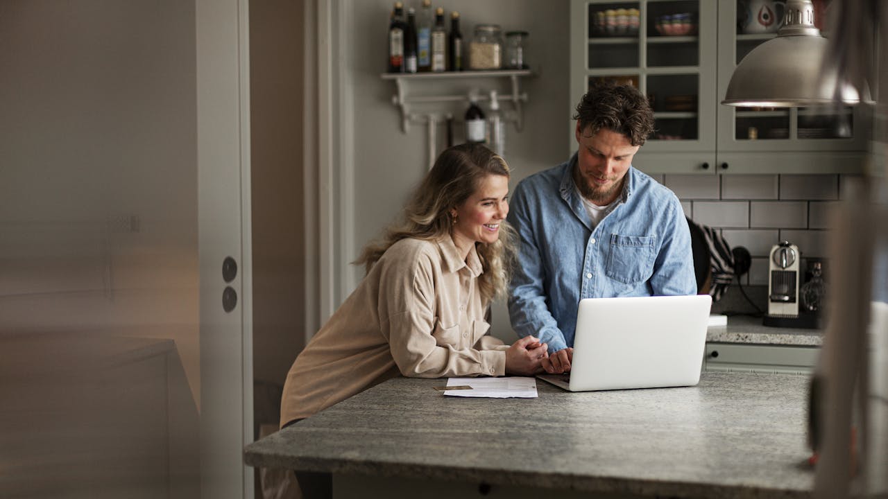 Kvinne og mann ser på laptop i et kjøkken