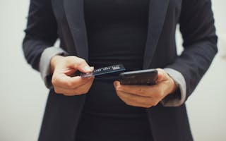 Kvinne med blazer holder mobiltelefon og bankkort i hendene