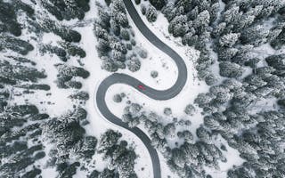 Rød bil på vei mellom trær i vinterlandskap