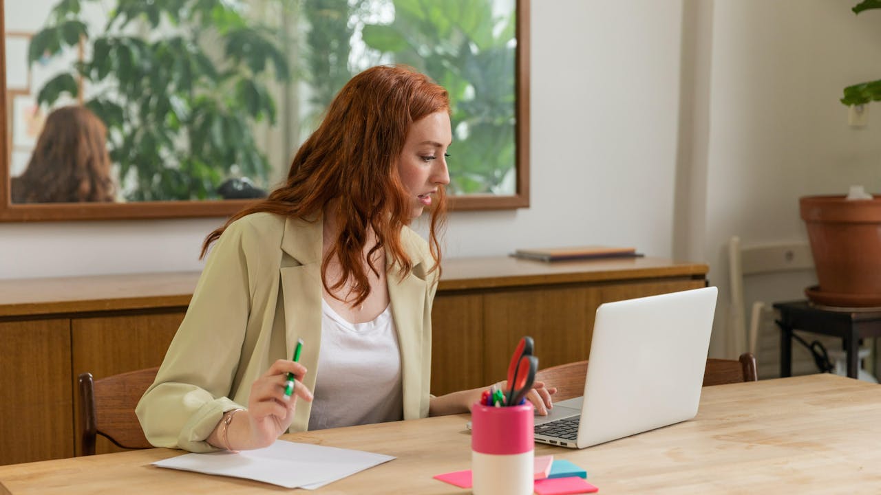Kvinne sitter ved skrivebord med datamaskin og skriveblokk