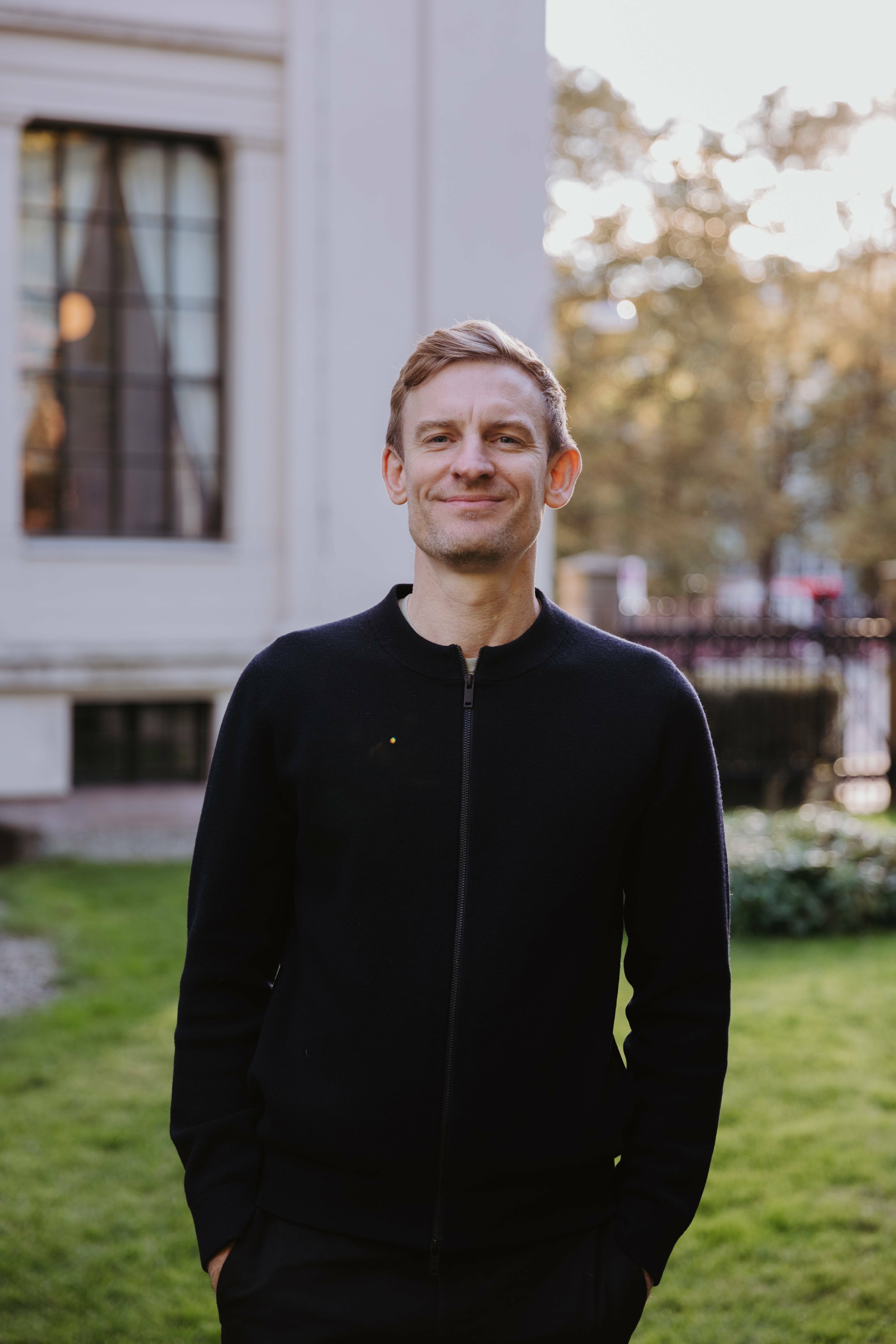 Mann i sorte klær ser i kameraet og smiler forsiktig