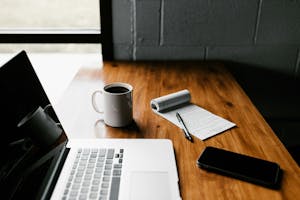 Skrivebord med laptop, kaffekopp og notatblokk