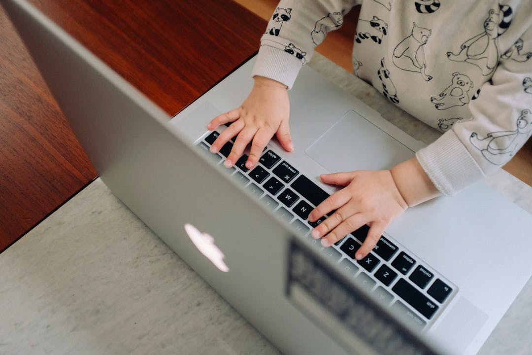 Et barn har hendene på tastaturet til en bærbar datamaskin