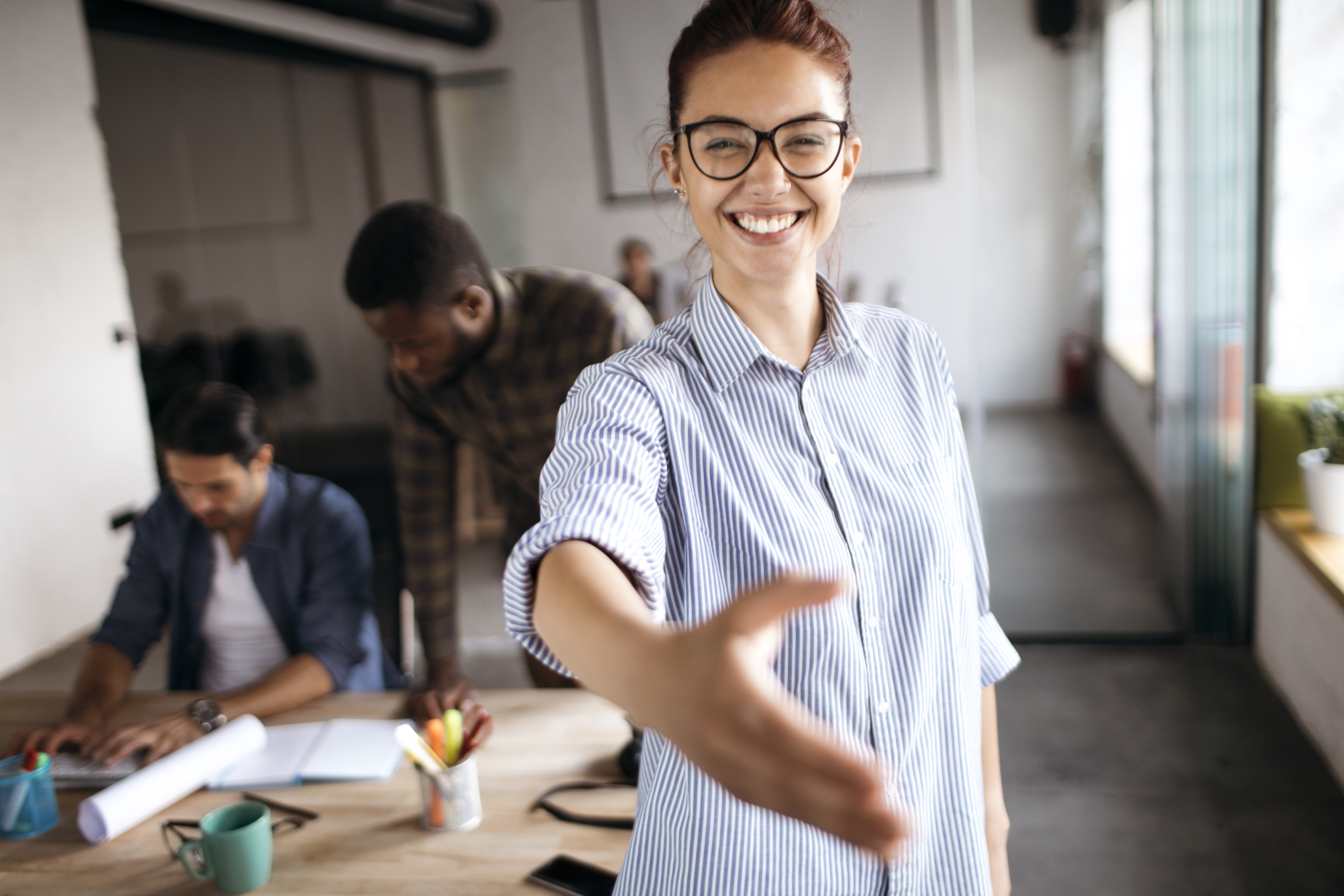 Kvinne i stripete skjorte strekker ut hånden til en hilsen i kontorlokaler